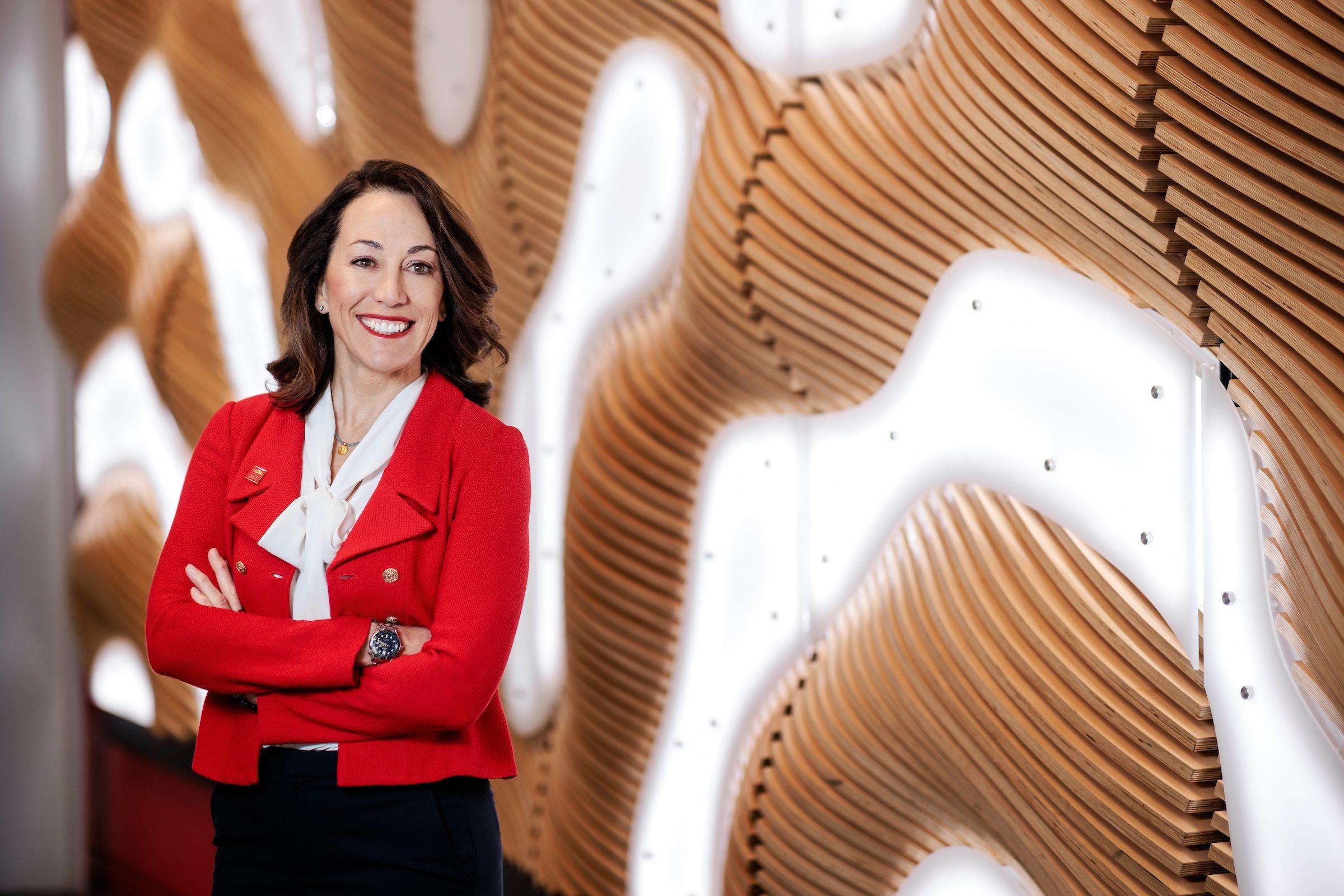 President Janine Davidson wearing a red blazer in front of an illuminated background.